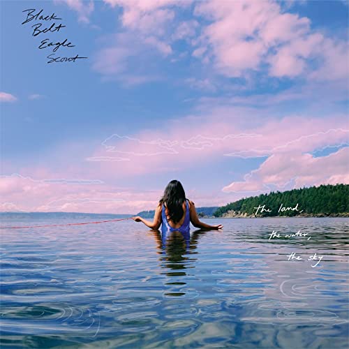 Woman in water facing the ocean under a cloudy, pink sky.