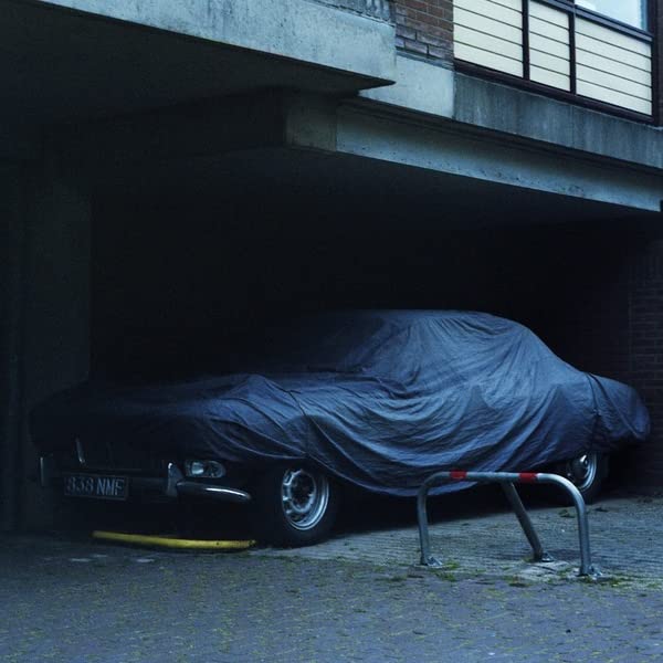 Covered car parked under a concrete building, dark and moody lighting.