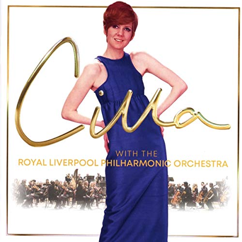 Cilla Black in a blue dress with an orchestra in the background.