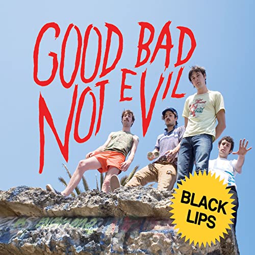 Four band members stand on a rocky ledge against a bright blue sky.