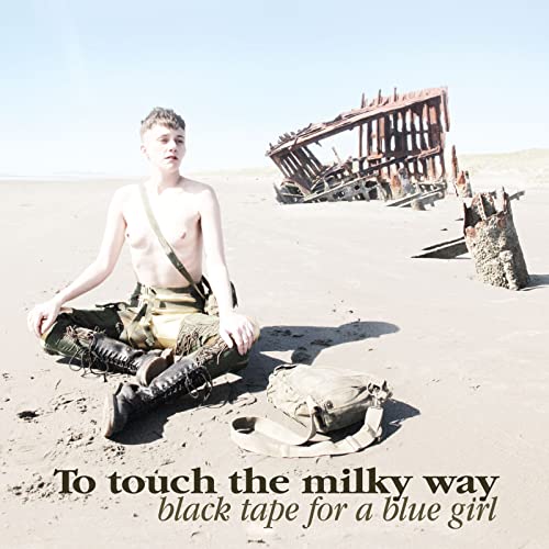 A person sits on a sandy beach near a shipwreck with text at bottom.