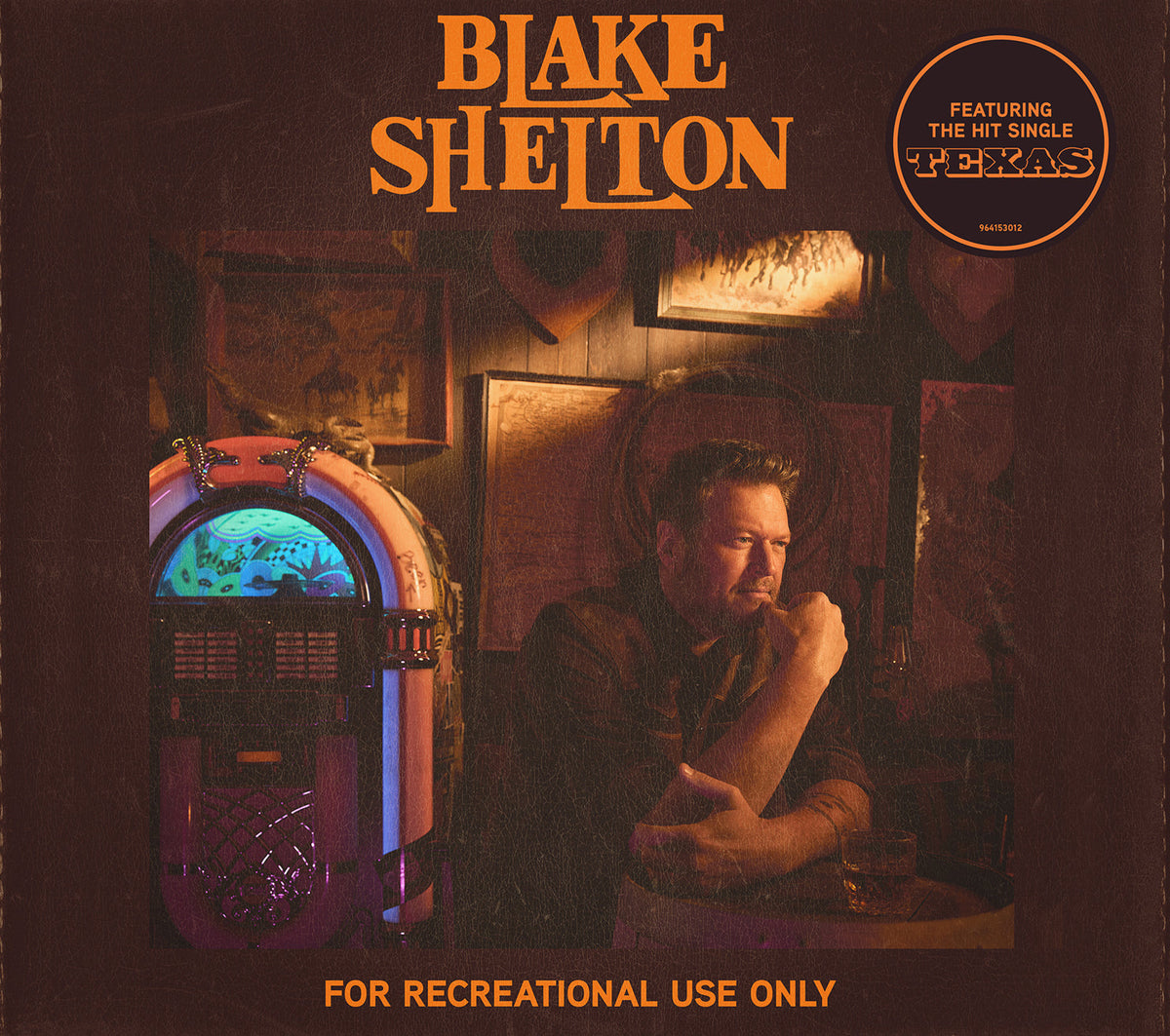 Blake Shelton sits beside a glowing jukebox in a dimly lit room.