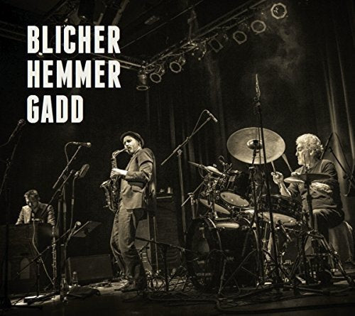 "Album cover featuring a black-and-white photo of three musicians performing on stage with instruments."