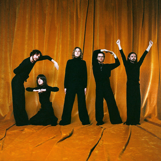 Four people in black clothing pose with raised arms against orange curtains.