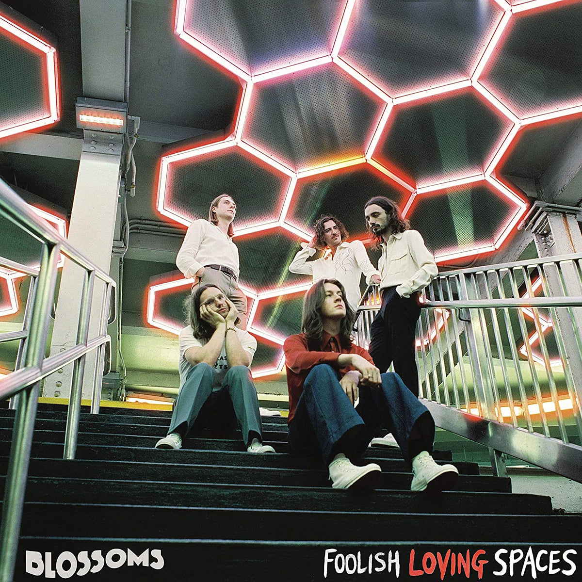 "Album cover: five band members on stairs under glowing hexagonal lights, 'Blossoms' and 'Foolish Loving Spaces'."