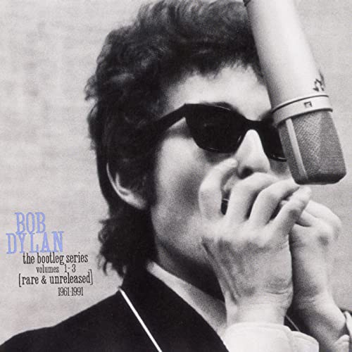 Black and white photo of Bob Dylan wearing sunglasses and playing a harmonica.