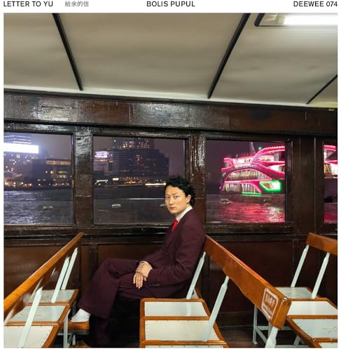 Man in a suit sits on a school desk before city lights.