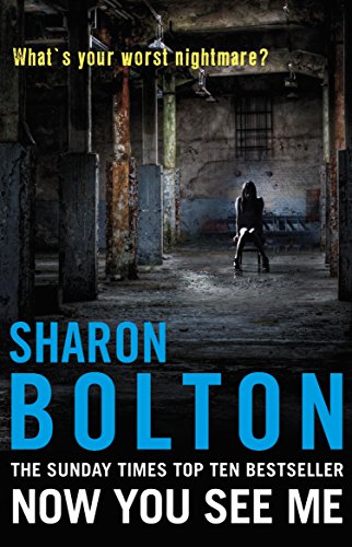 A woman sits on a chair in a dark, industrial, warehouse-like setting.