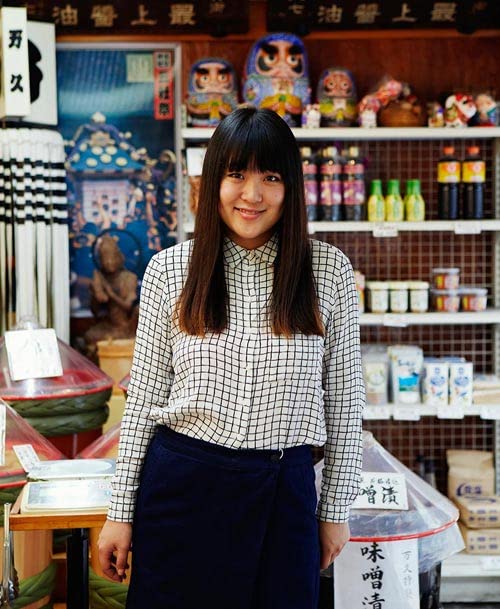 Young woman in a checkered shirt stands in front of Japanese goods.