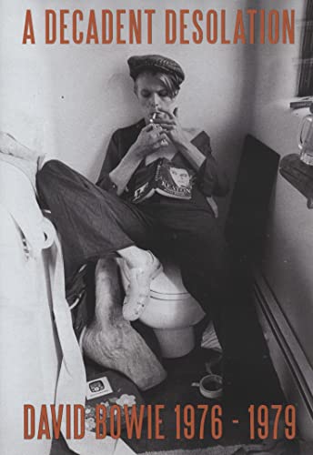 Black and white photo of David Bowie sitting on a toilet wearing a cap.