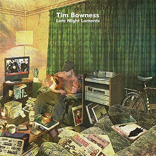 "Album cover with man sitting in a cluttered room, surrounded by papers and media."