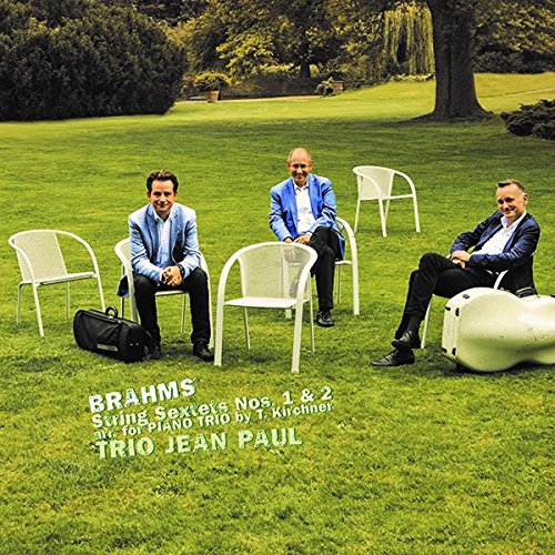 Three musicians seated on chairs in a green garden setting.