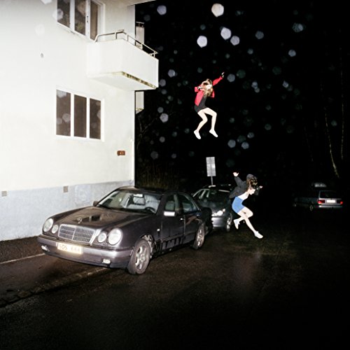 People levitating and jumping near a car and building at night.