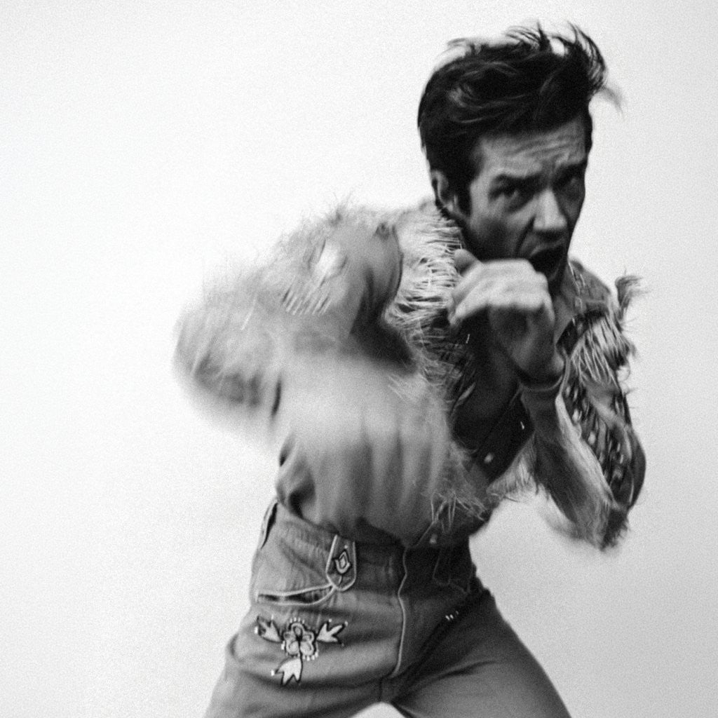 Black and white photo of Brandon Flowers throwing a punch in a fringed shirt.