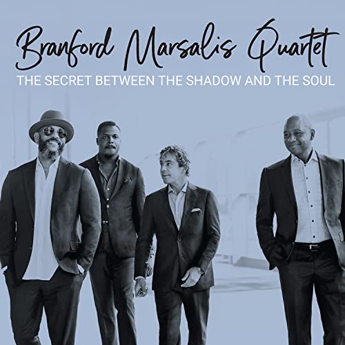 Four men in suits standing against a light blue background, album cover art.