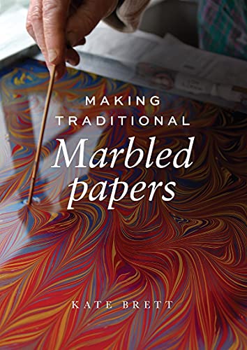 A hand uses a stylus to create swirling patterns in colorful marbled paper liquid.