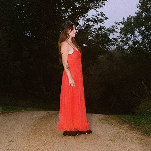 Woman in red dress and hat standing on a dirt road.