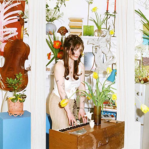 Woman with brown hair playing a keyboard in a room filled with plants.