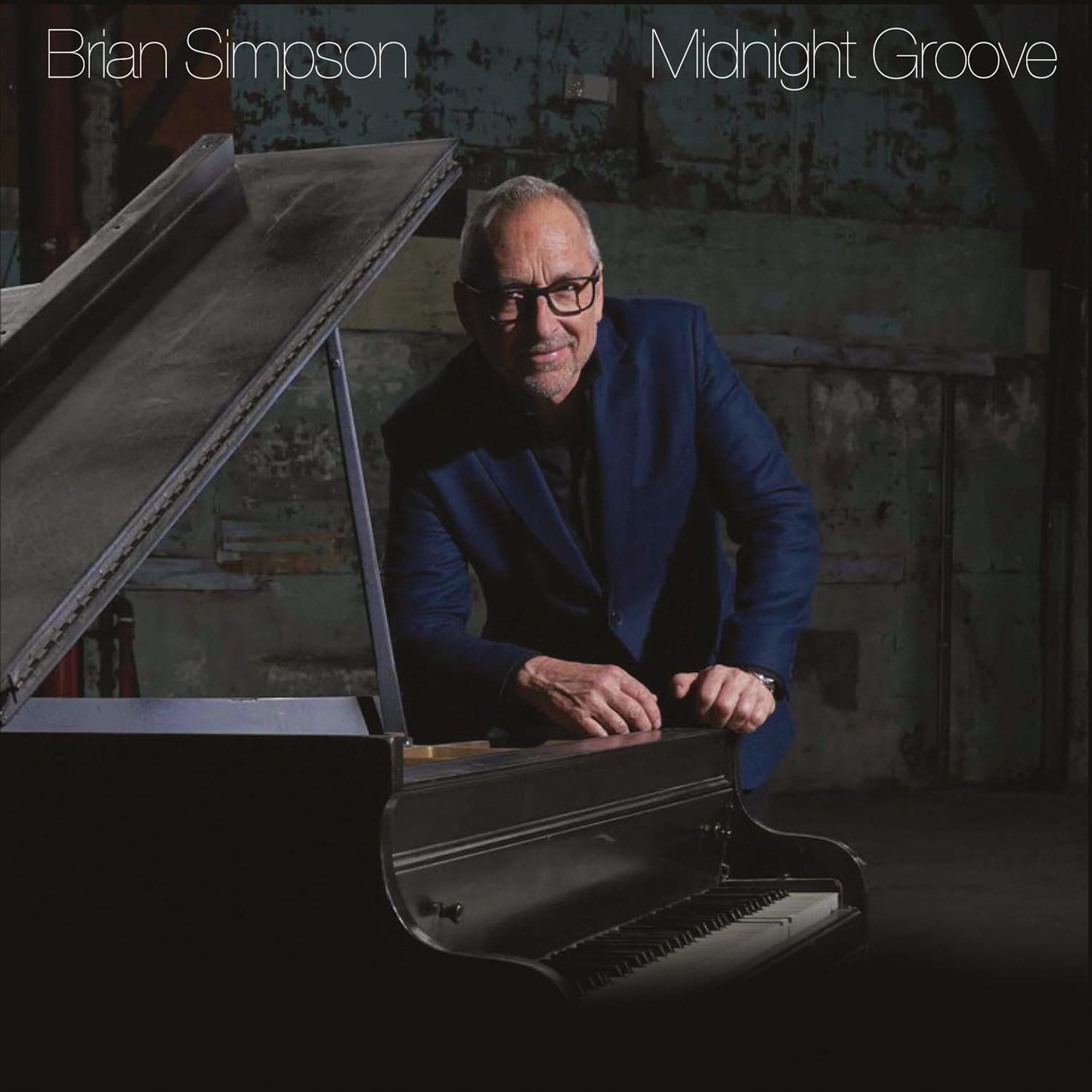Brian Simpson in a blue blazer leaning over a grand piano in a studio.