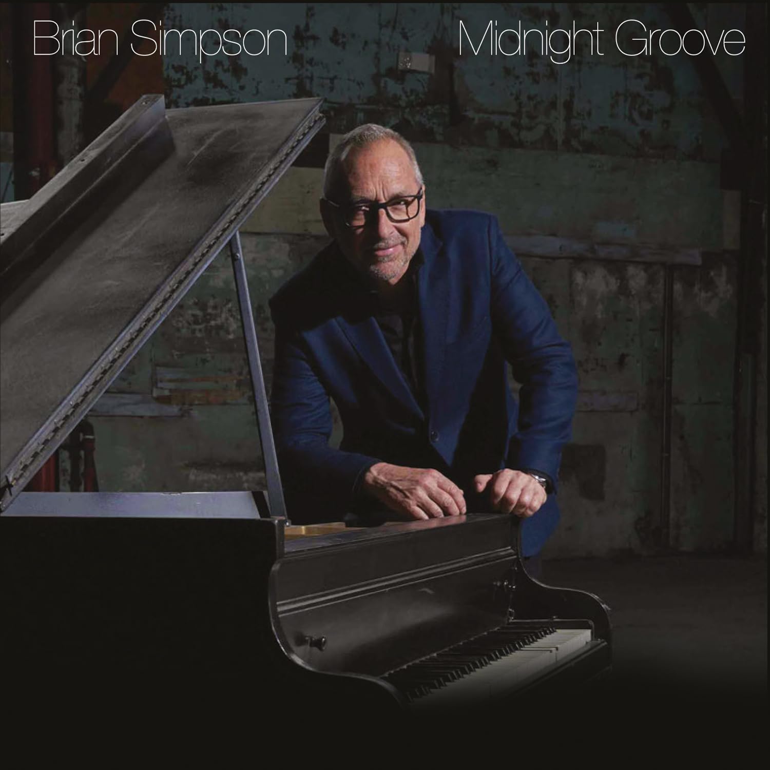 Brian Simpson in a blue blazer leaning over a grand piano in a studio.
