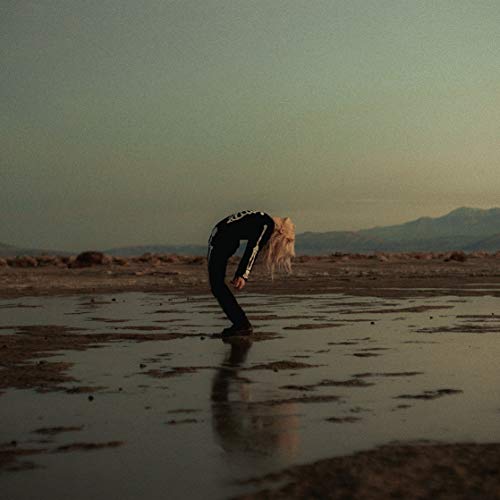 A person in a skeleton suit arches backward in a shallow, muddy desert landscape.