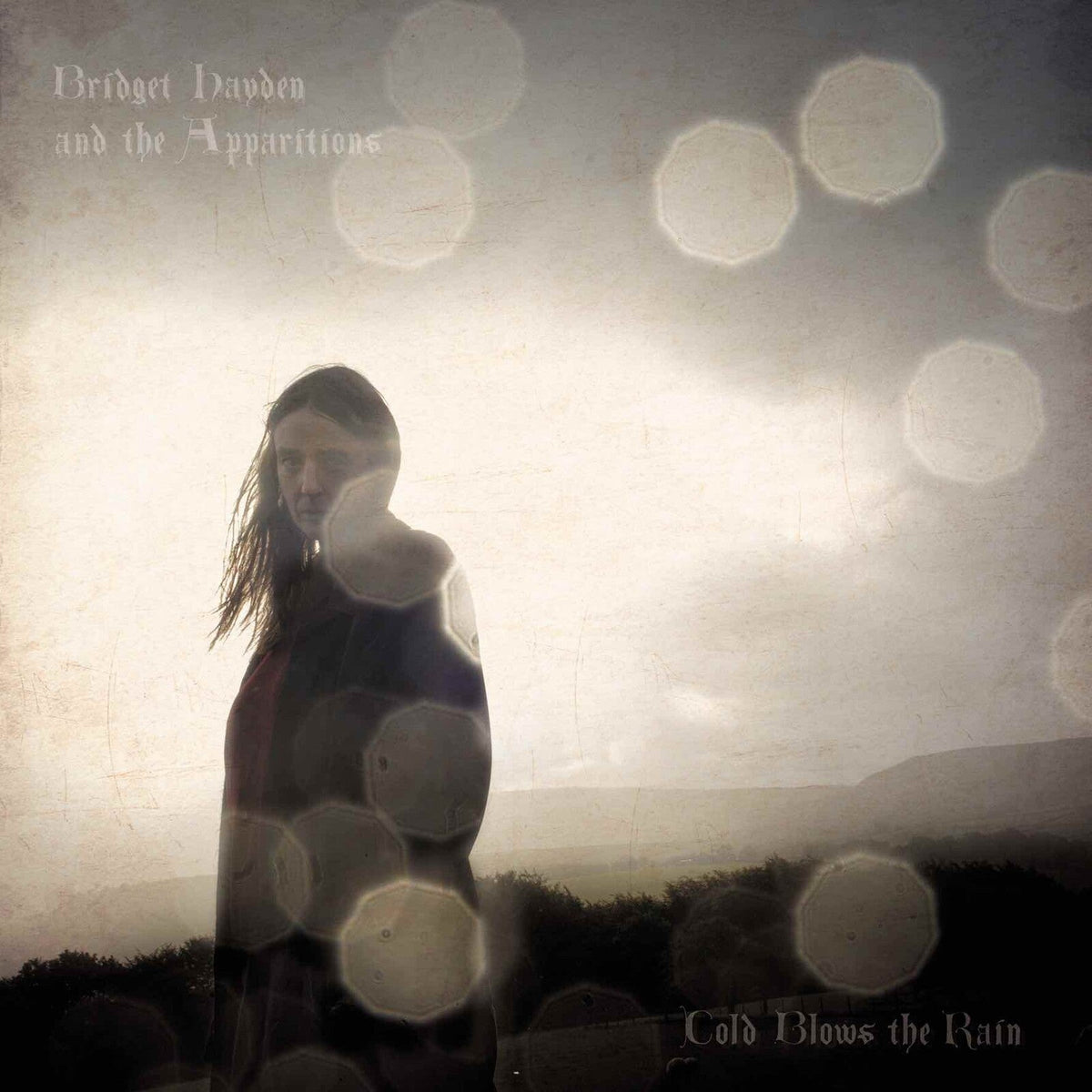 Album cover: woman in a dark coat, blurred, with circular light flares.