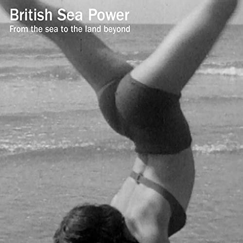 Black and white photo of a person doing a handstand on a beach.