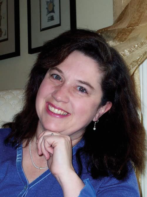Woman with dark curly hair smiling, wearing a pearl necklace.