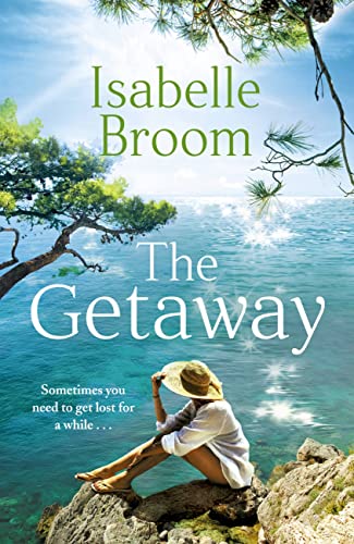 A woman in a sun hat sits on rocks overlooking a sparkling blue sea.