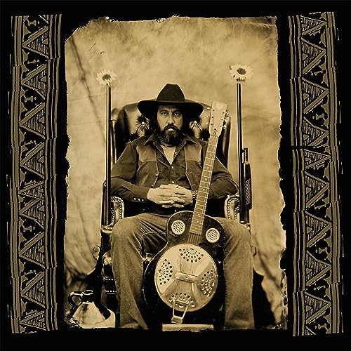 Bearded man with guitar sits in ornate chair, sepia tone.