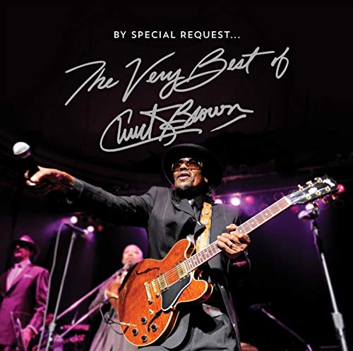 "Chuck Brown holding a guitar and microphone on stage, with band members in the background."