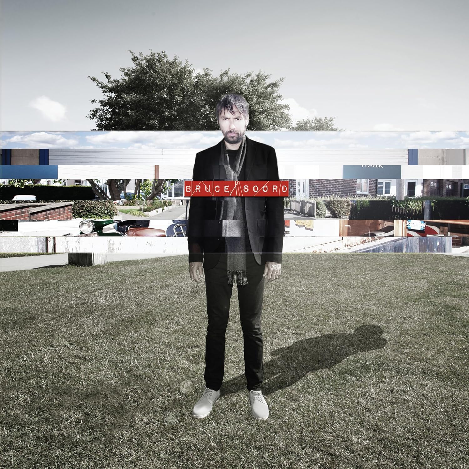 Man in black suit standing on grass with building backdrop.