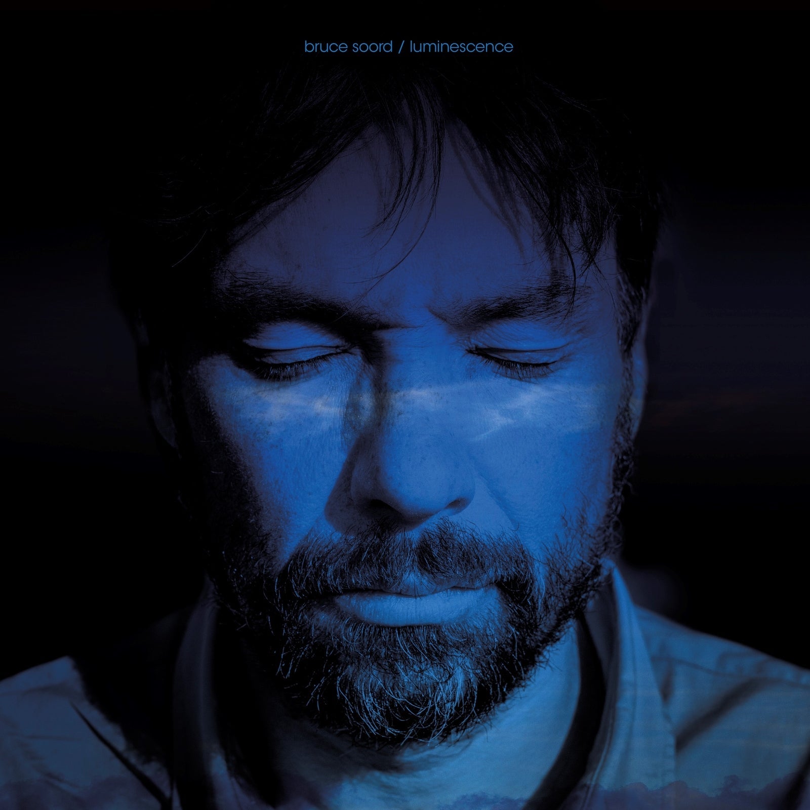 Close-up portrait of a man with blue light reflecting on his face.
