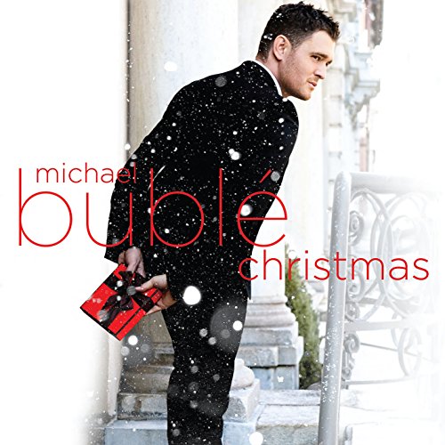 Michael Bublé in a black suit holding a wrapped gift on a snowy staircase.