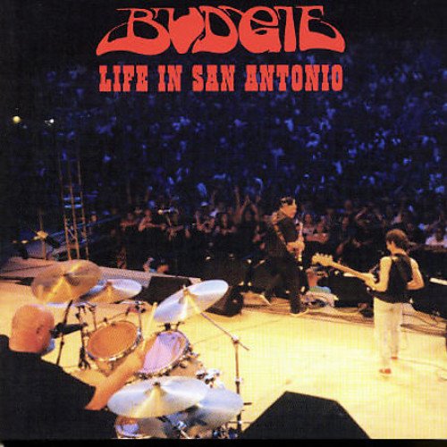Budgie band performing live on stage with a drummer in the foreground.