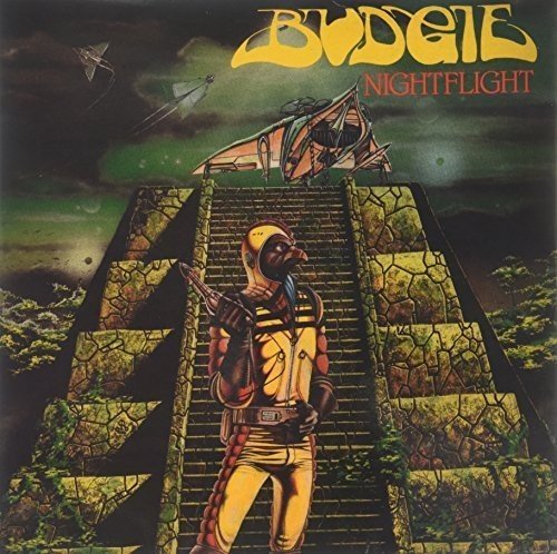 A bird-headed figure stands before a stone pyramid with a spaceship overhead at night.