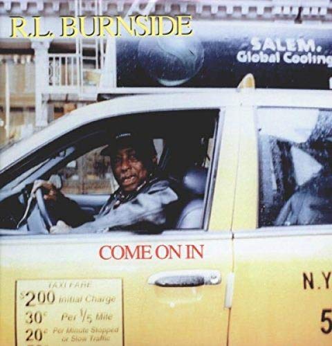 R.L. Burnside sitting in the driver's seat of a yellow New York City taxi.