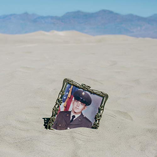 A gold locket containing a soldier's portrait is half-buried in desert sand.