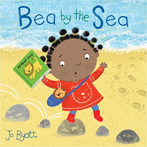 Child with dark skin reading a book on a sandy beach.