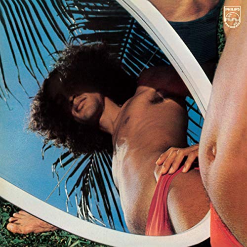 A man with curly hair is reflected in a circular mirror outdoors.
