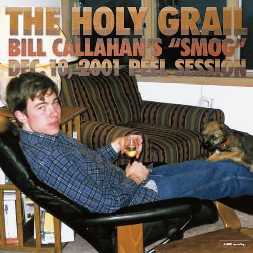 Bill Callahan sits in a recliner holding a glass with a small dog nearby.