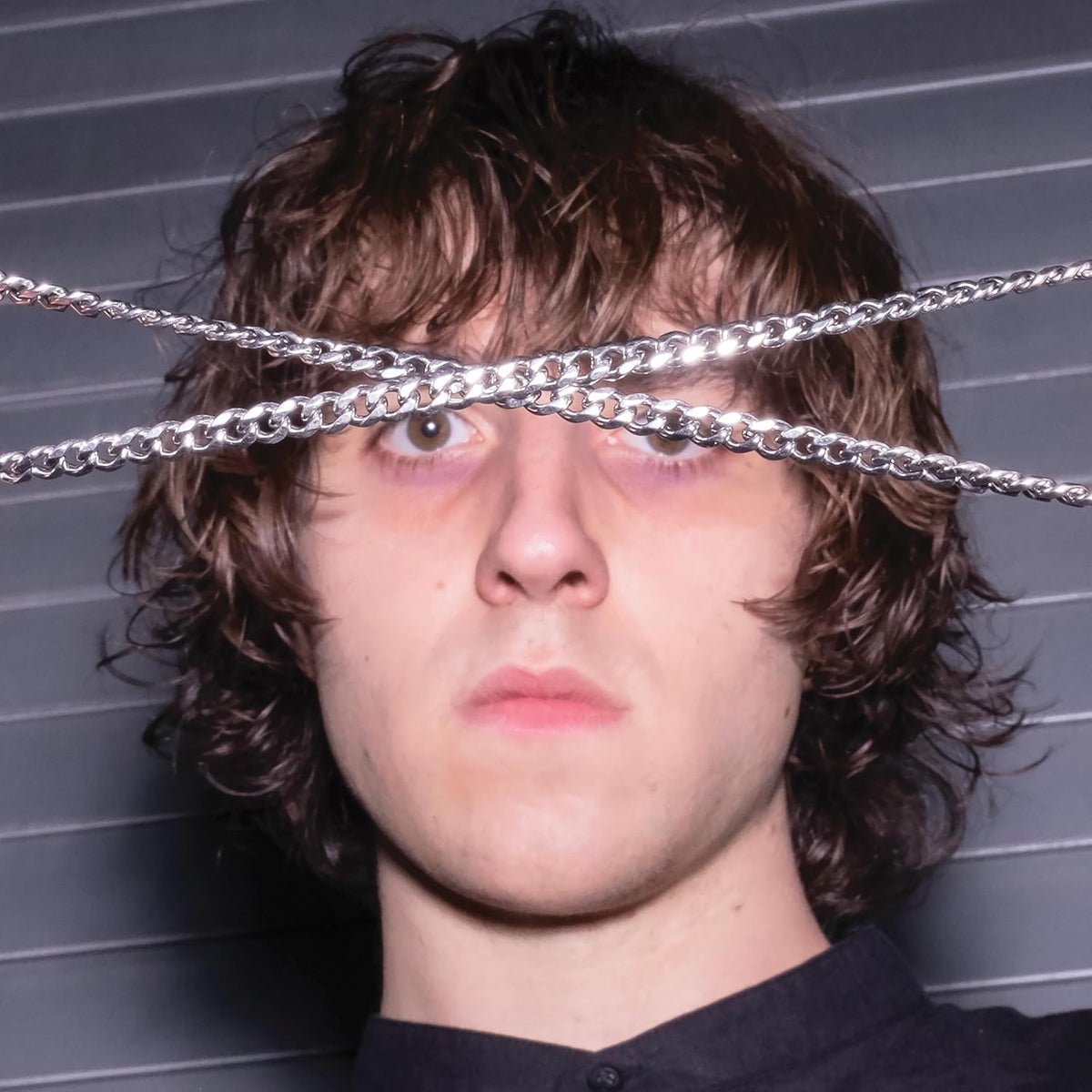 Close-up of a young man with curly hair and silver chains over eyes.