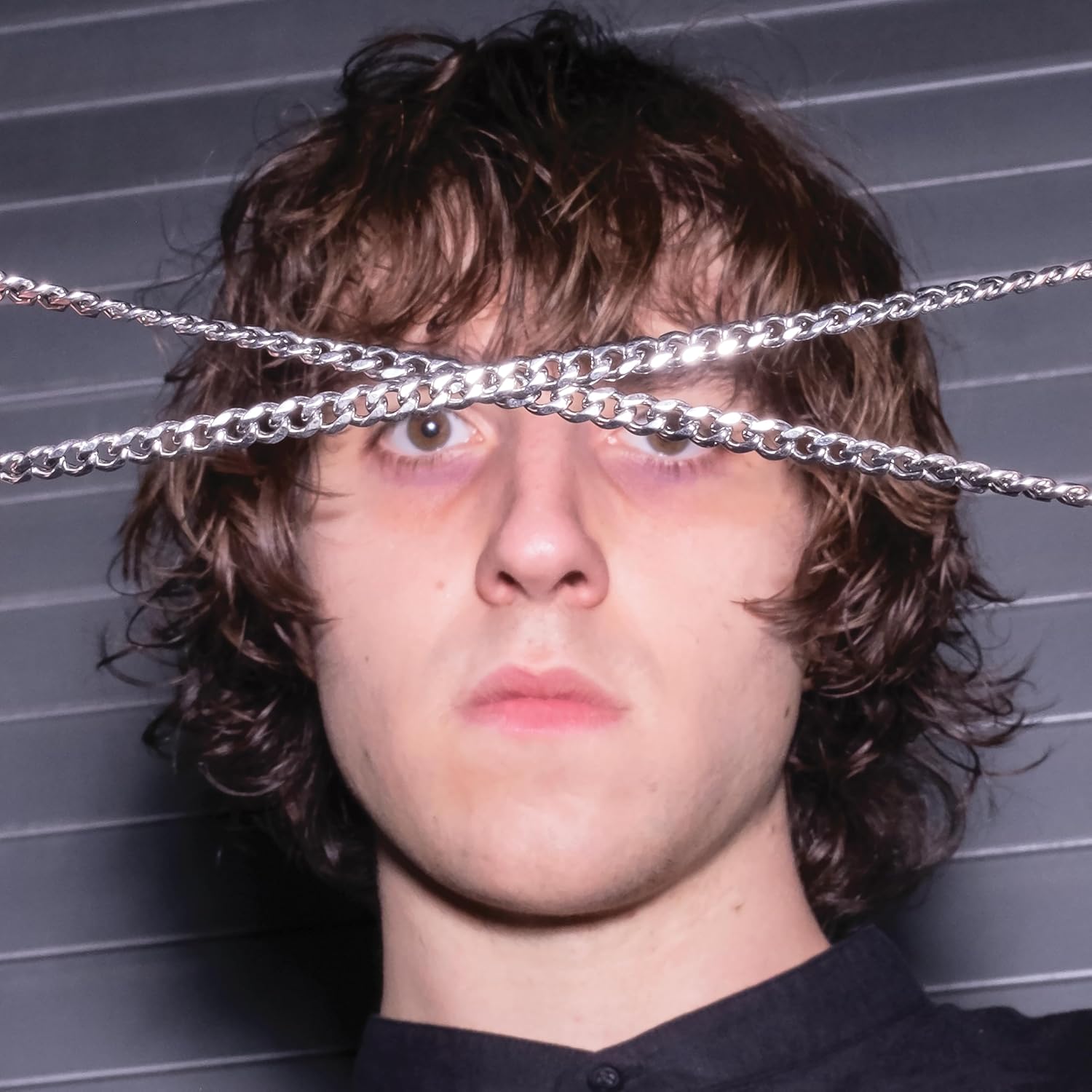 Close-up of a young man with curly hair and silver chains over eyes.