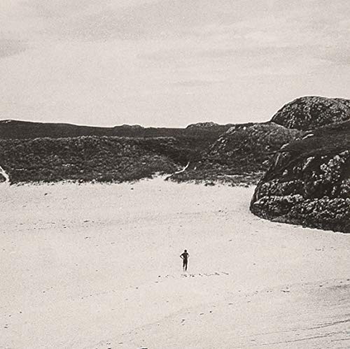 Black and white landscape with a lone figure on a sandy beach.