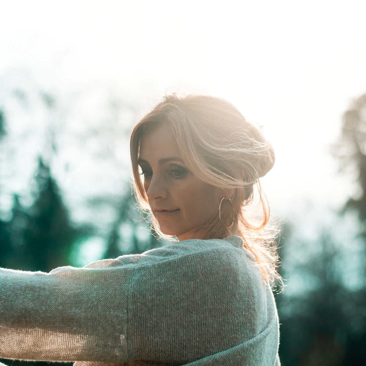 Close-up of a blonde woman in a grey sweater looking away outdoors.