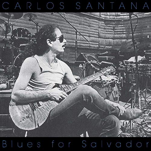 Carlos Santana seated, playing guitar on stage, album cover.