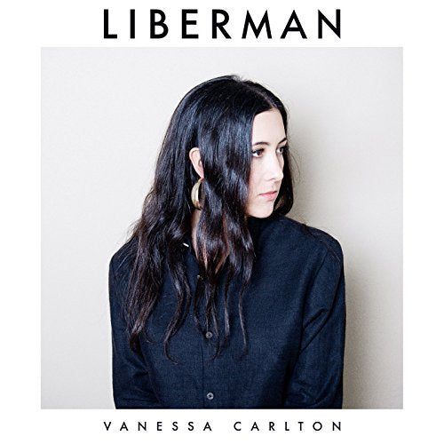Woman with long black hair and dark shirt on album cover with white background.