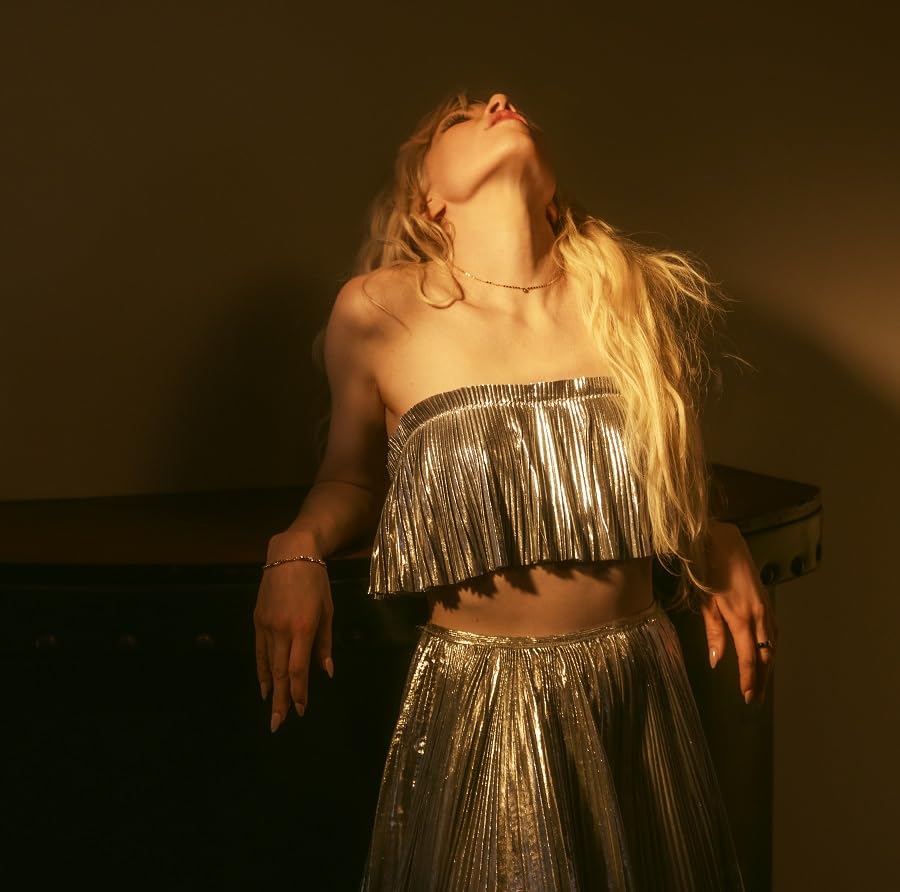 Carly Rae Jepsen in silver outfit, looking upwards in warm lighting.