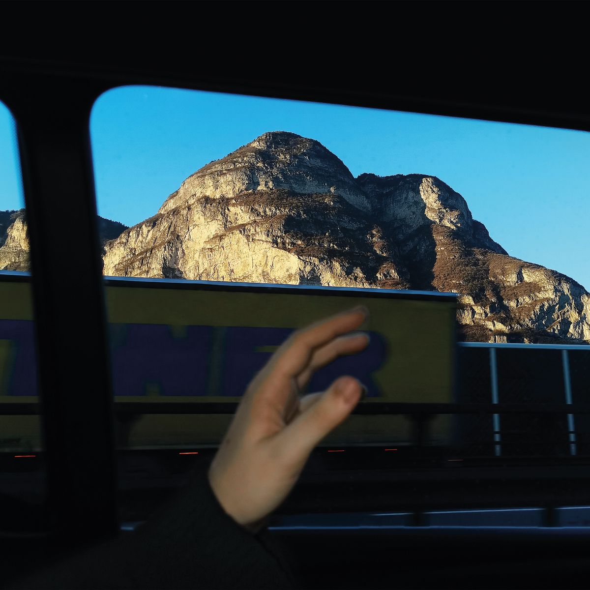 Mountain view framed by a car window and a reaching hand.