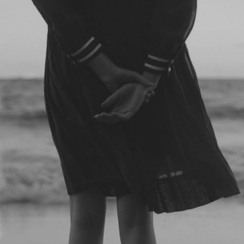 Person with hands clasped behind back, wearing a dark, pleated dress.
